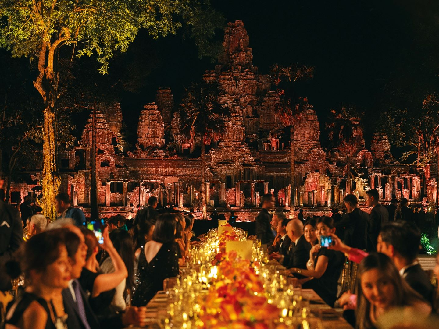 A candlelit gala dinner set before the illuminated towers of Bayon Temple at Angkor Wat