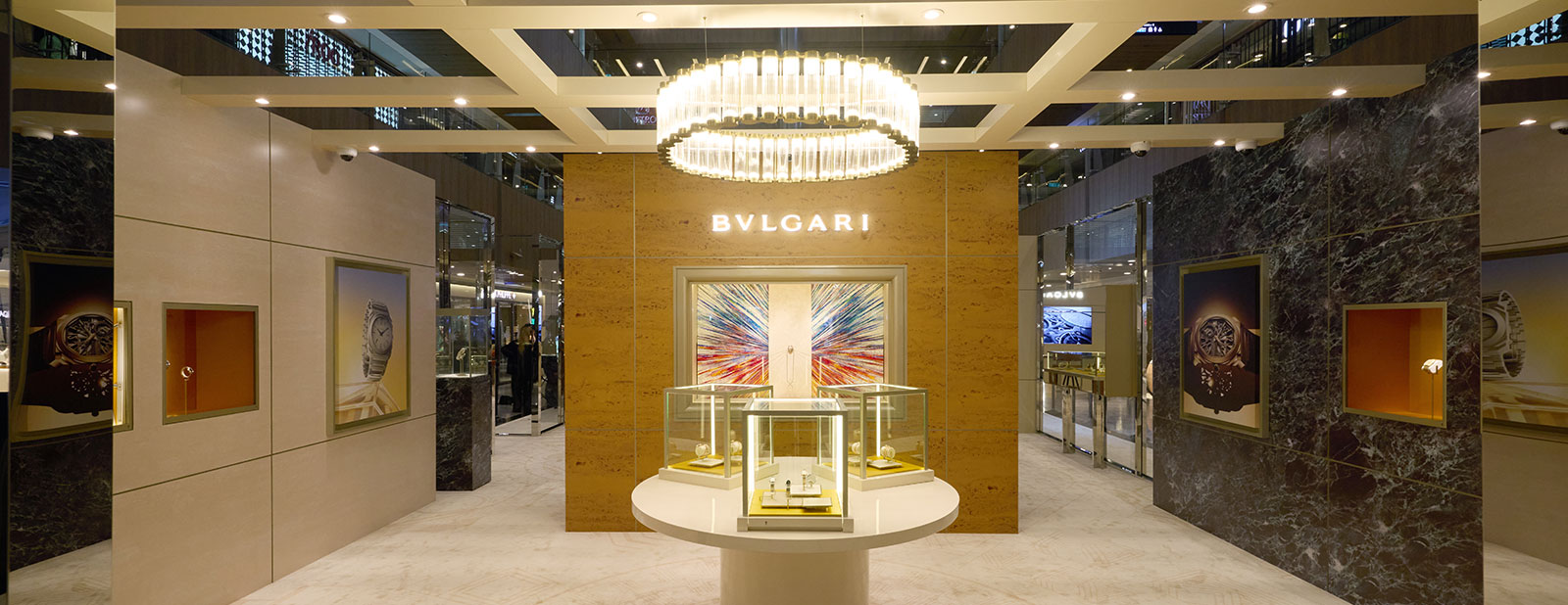 A BVLGARI pop-up boutique with an illuminated circular chandelier, glass display cases and a backlit BVLGARI sign
